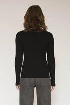 A woman viewed from the back wearing a fitted black long-sleeve knit top and gray pinstriped trousers against a plain light background.
