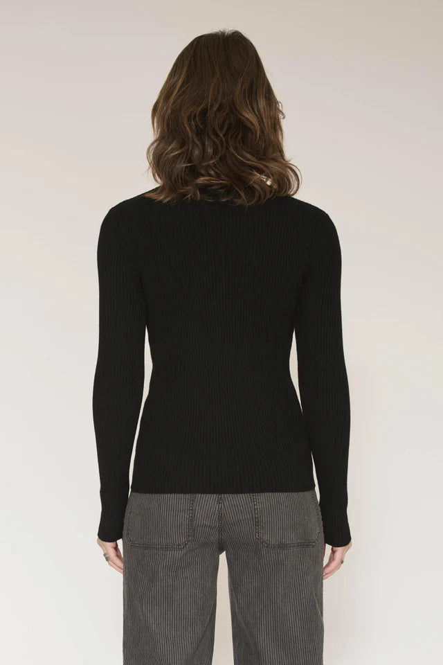 A woman viewed from the back wearing a fitted black long-sleeve knit top and gray pinstriped trousers against a plain light background.