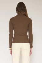 A woman shown from the back wearing a ribbed brown mock neck sweater and cream pants against a plain light background.