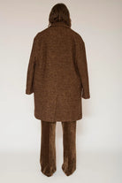A model viewed from the back wearing a brown textured tweed coat and matching brown wide-leg trousers against a plain off-white studio background.
