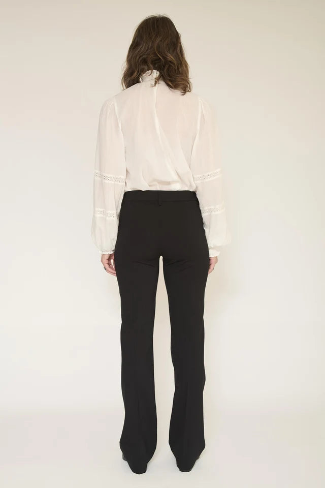 A woman shown from the back wearing a white long-sleeve blouse with sheer sleeves and black high-waisted flared trousers, photographed against a plain light background.