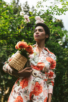 Woman in a floral dress holding flowers and a basket in a garden setting