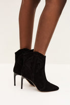 Black high-heeled ankle boots worn with sheer tights on a white background
