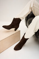Brown suede boots worn with white pants on a minimal white background