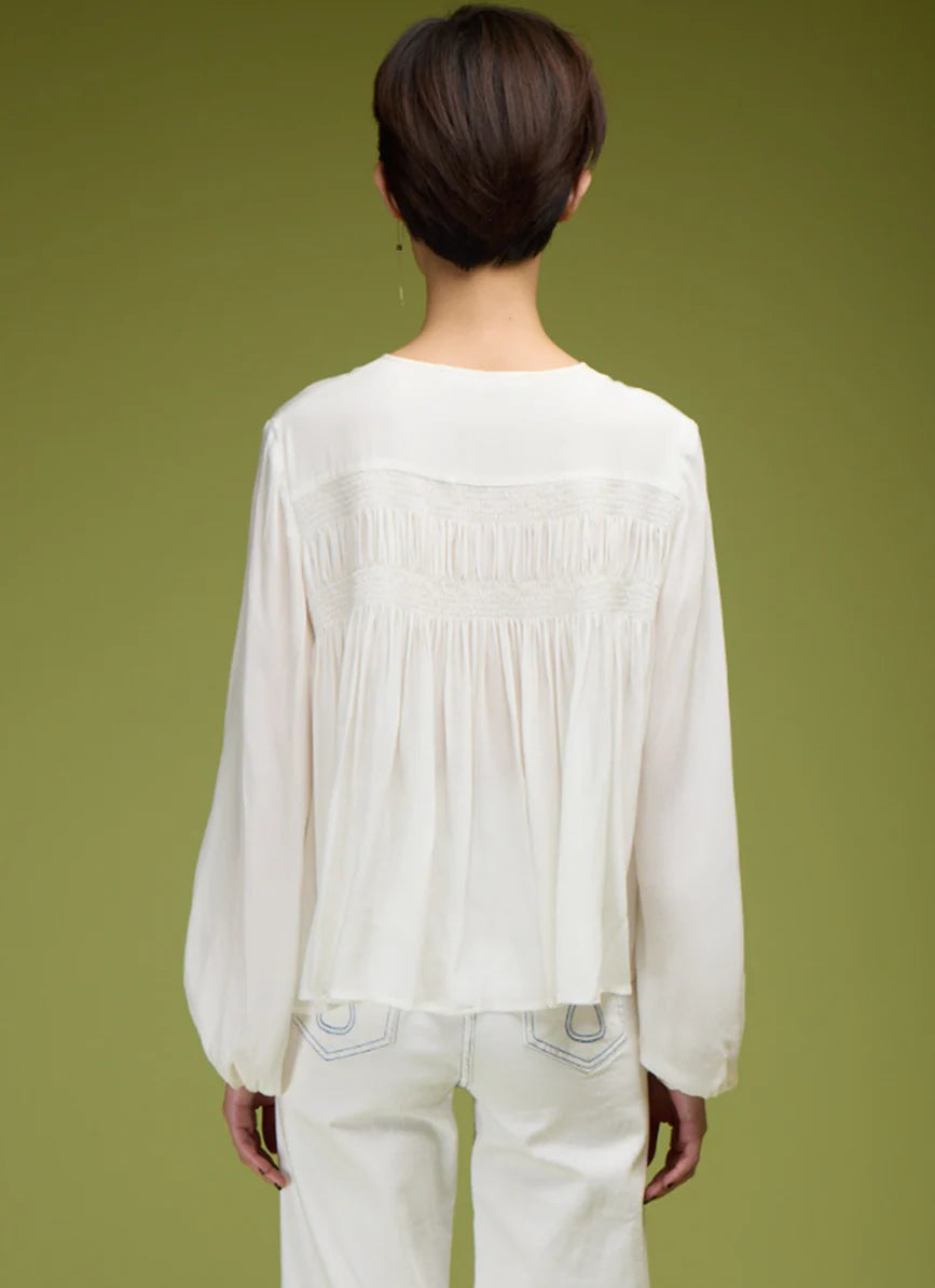 Person wearing a white blouse with long sleeves and a green background