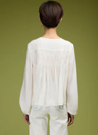 Person wearing a white blouse with long sleeves and a green background