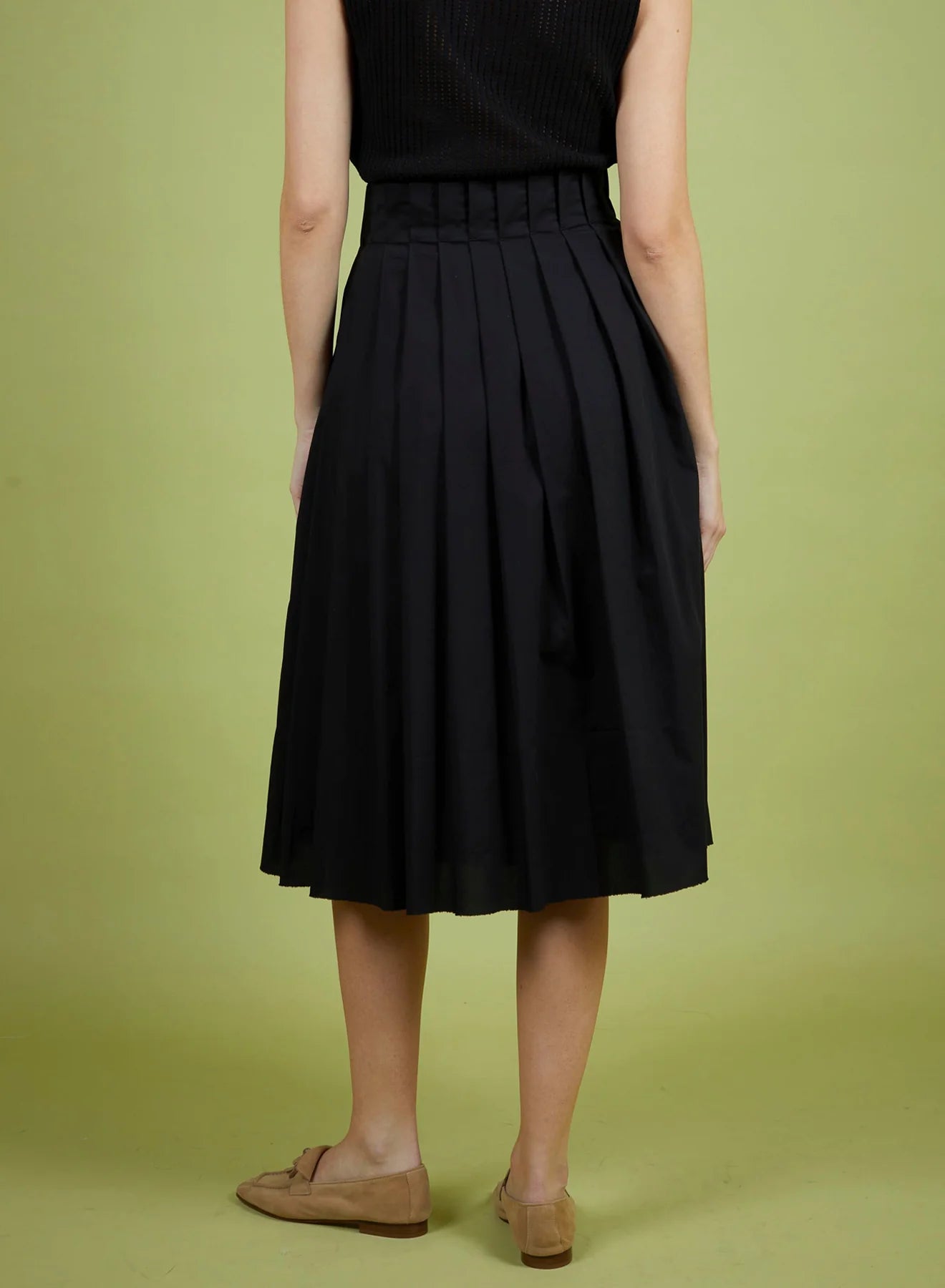 Person wearing a black pleated skirt on a green background