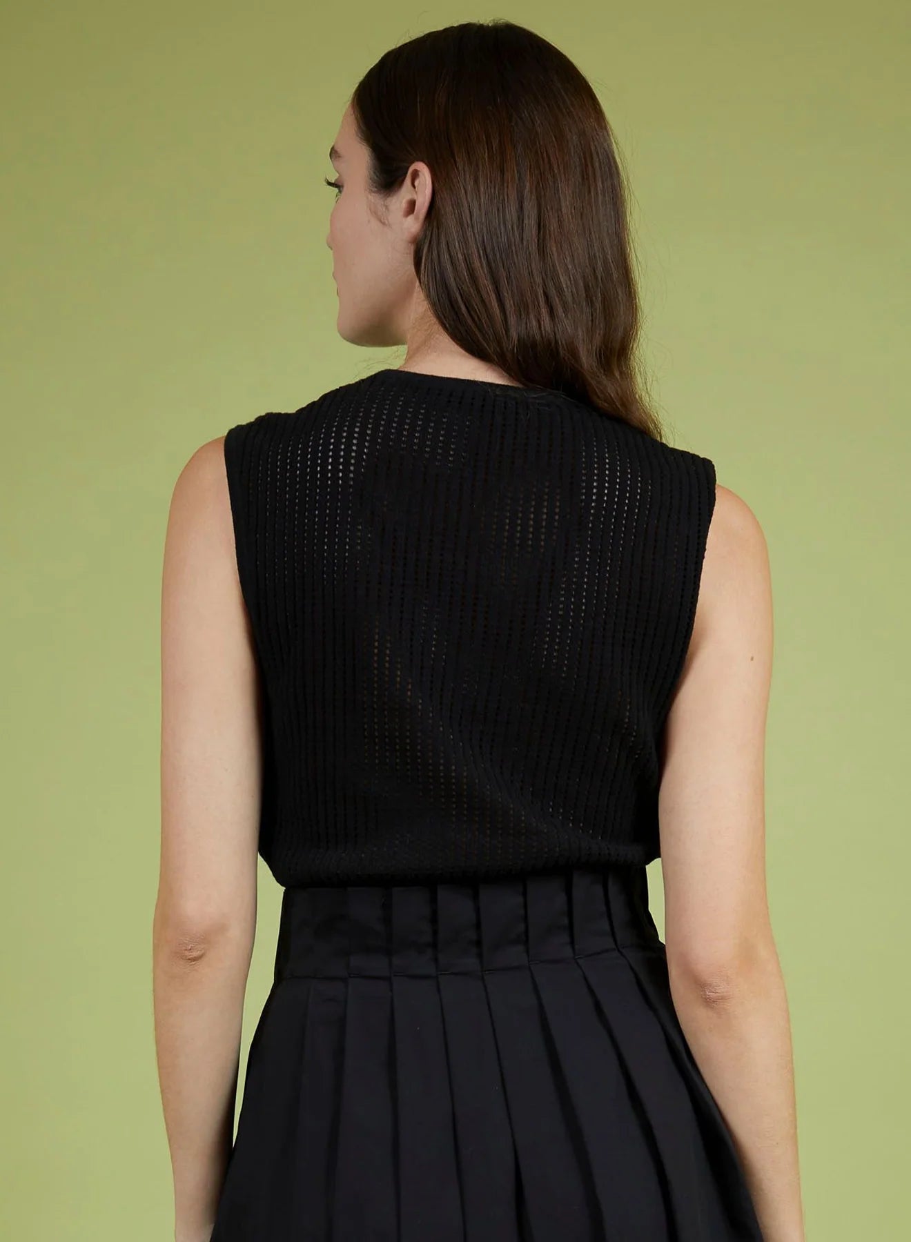 Woman wearing a black sleeveless top and skirt against a green background