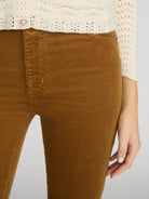 Close-up of a person wearing brown corduroy pants and a cream knit cardigan, cropped from the chest down against a light gray studio background.