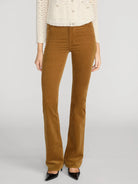 A model wearing a pair of brown corduroy flare pants, styled with a cream knit sweater and black pointed-toe heels, against a light gray studio background.