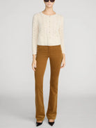 A model wearing a cream-colored textured knit cardigan, brown corduroy flare pants, and black pointed-toe heels, photographed against a neutral light gray studio background.