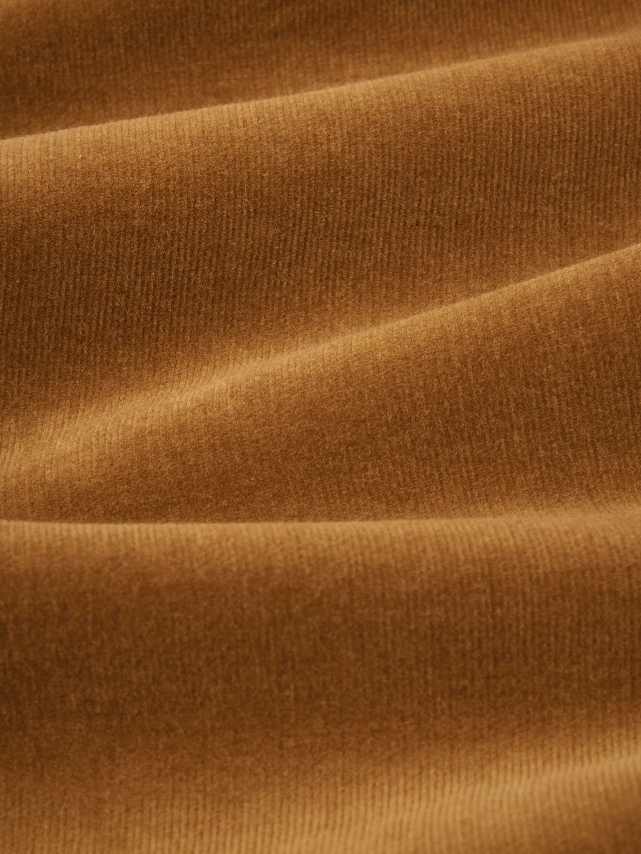 A close-up of draped ribbed fabric in a warm camel brown color, showing the texture and soft folds.