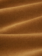 A close-up of draped ribbed fabric in a warm camel brown color, showing the texture and soft folds.