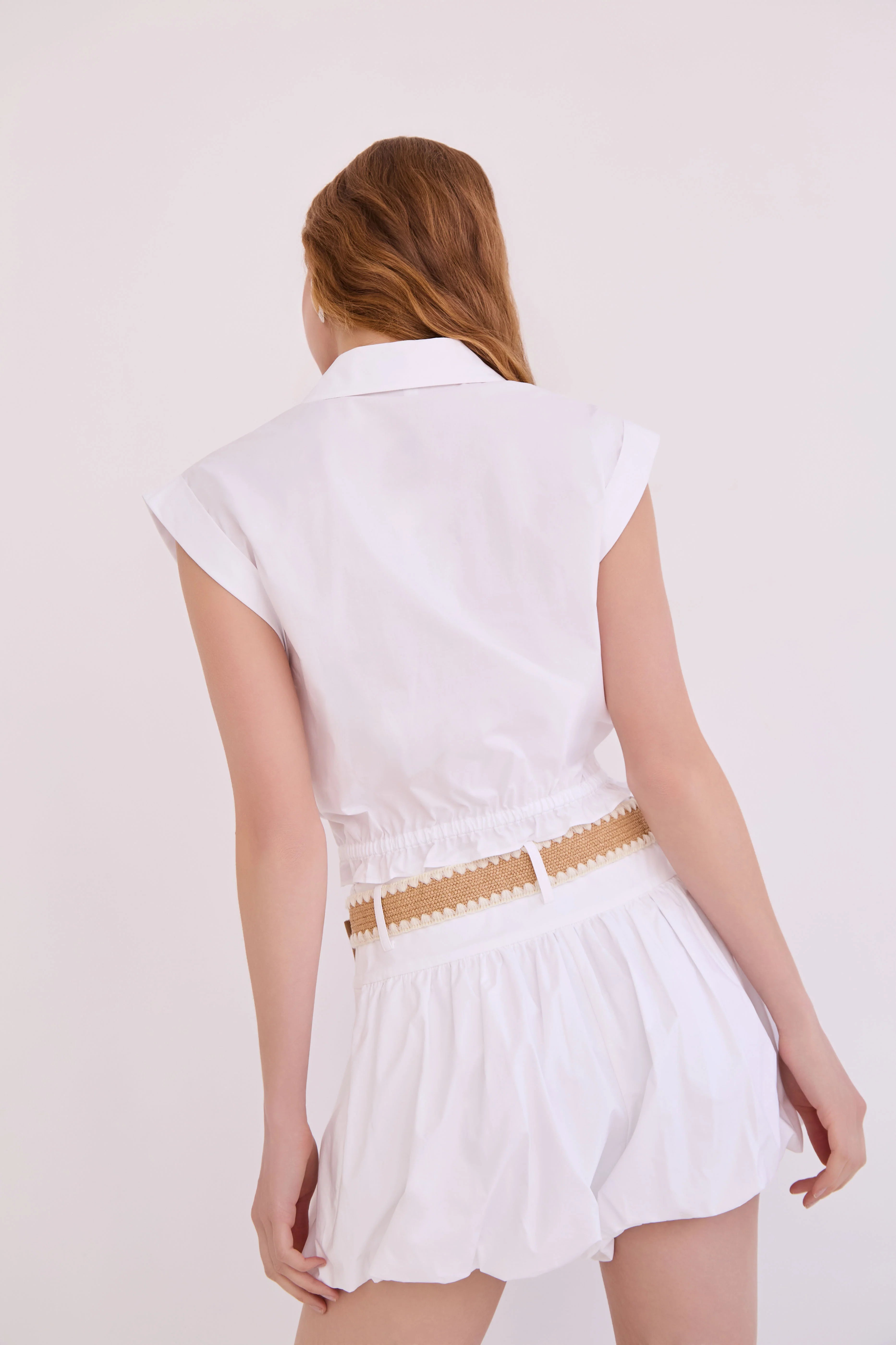 Woman wearing a white dress with a beige belt on a plain background