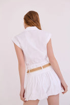 Woman wearing a white dress with a beige belt on a plain background