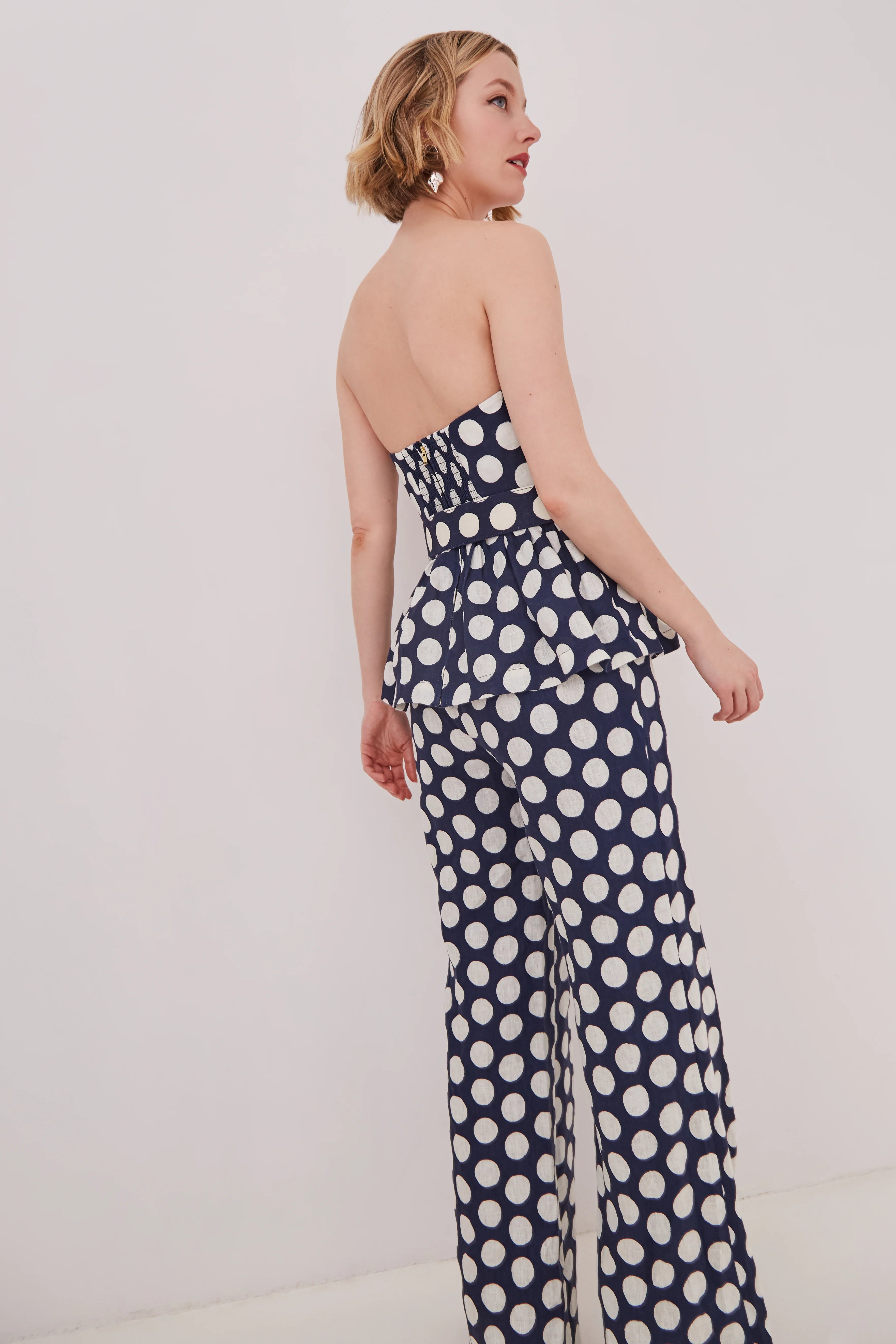 Woman wearing a strapless navy jumpsuit with white polka dots on a plain background
