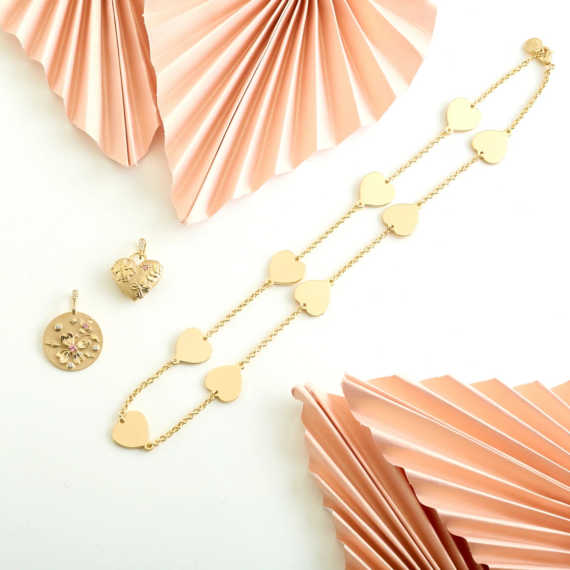 Gold heart-shaped necklace and earrings on a white background with pink decorative elements.