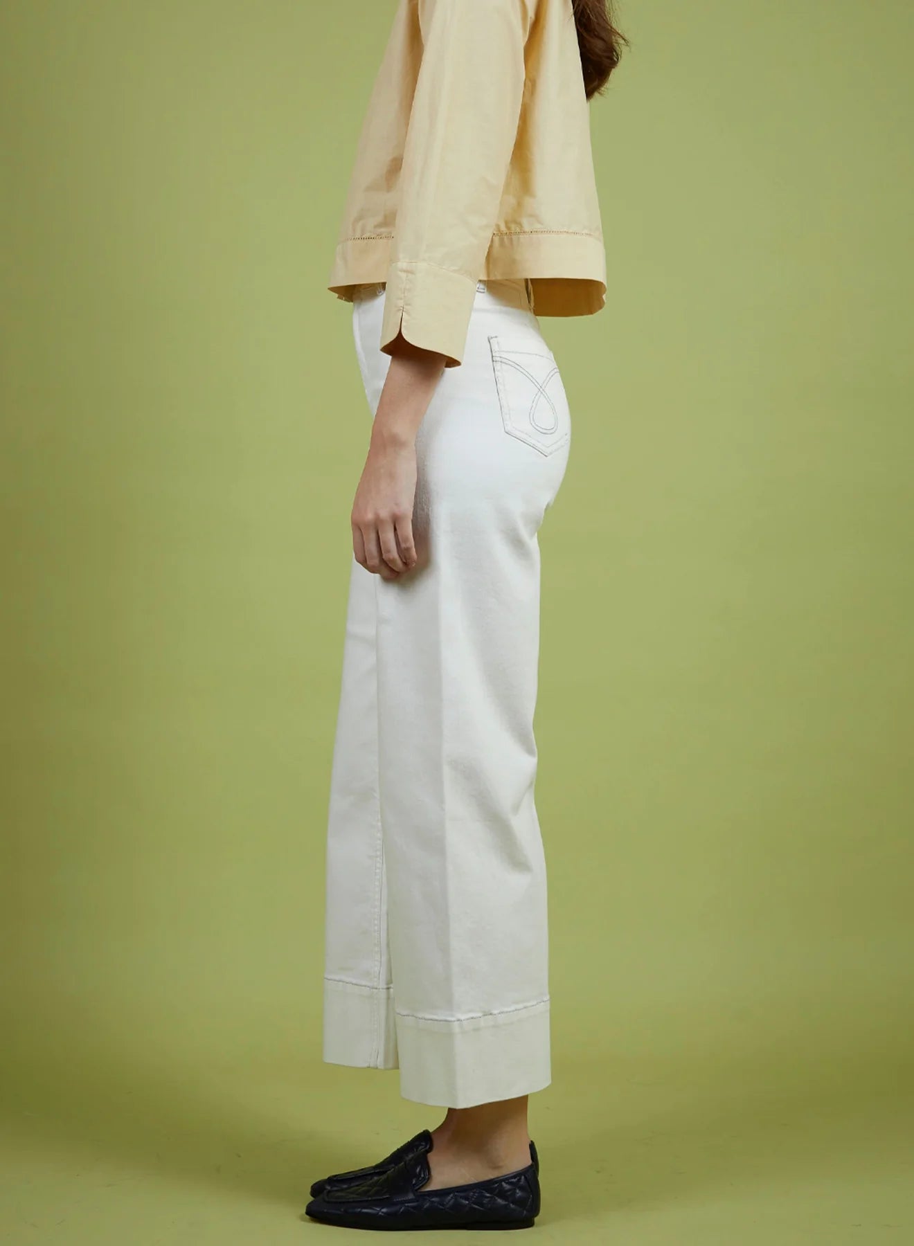 Person wearing a beige jacket and white pants on a green background