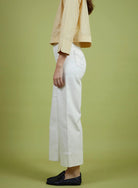 Person wearing a beige jacket and white pants on a green background