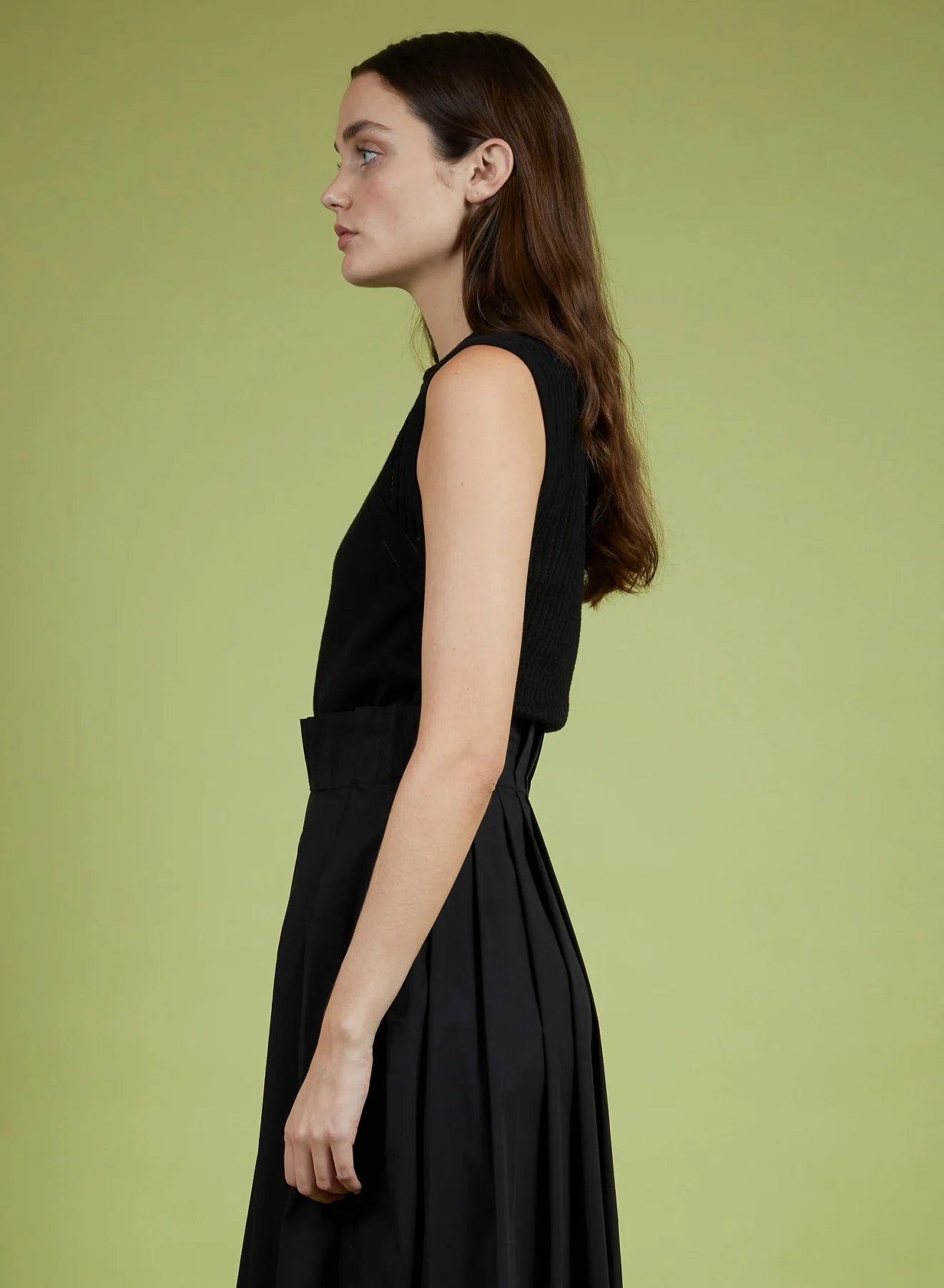 Woman wearing a black sleeveless top and black skirt against a green background