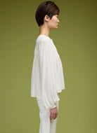 Person wearing a white blouse and white pants against a green background