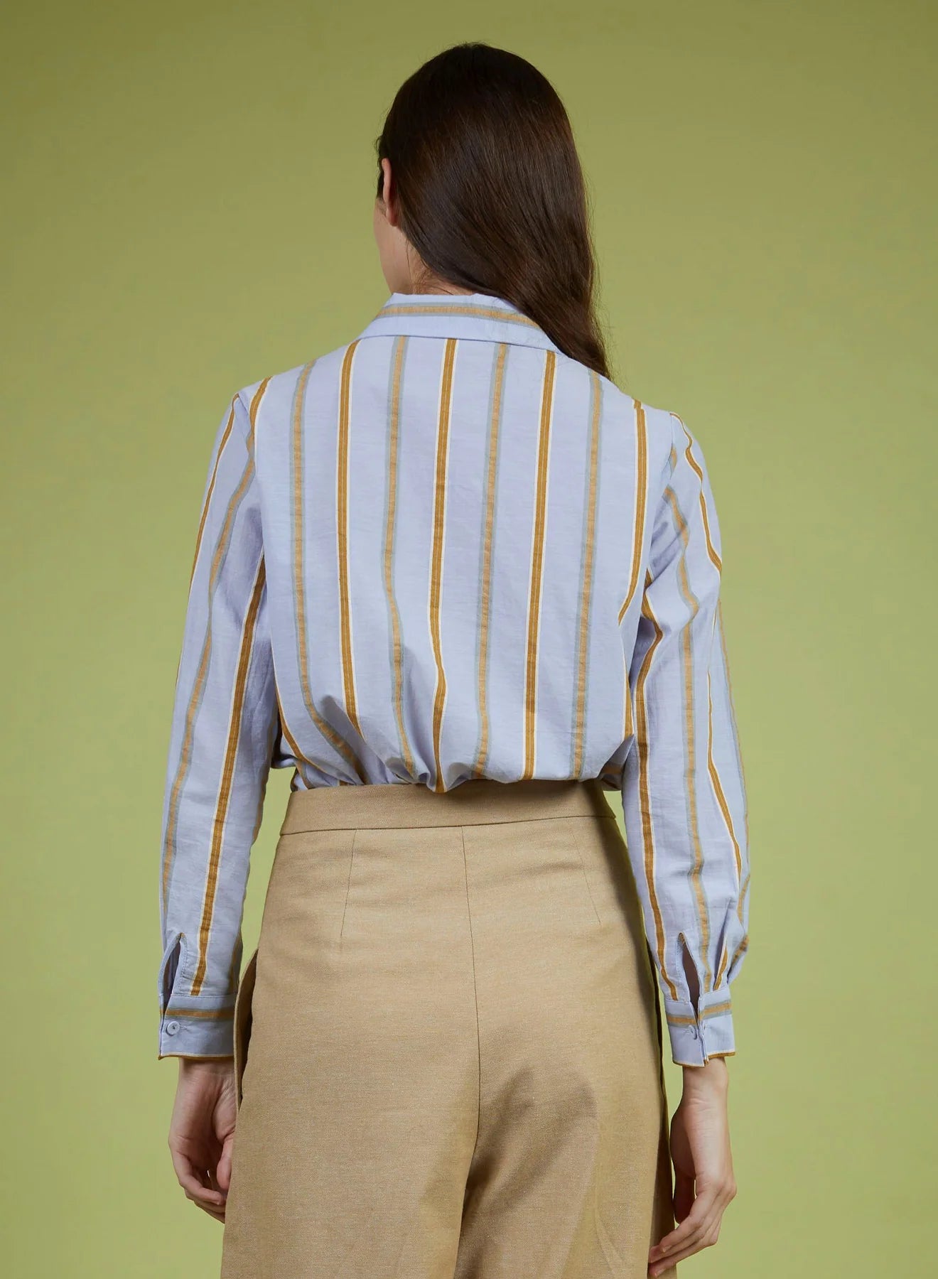 Person wearing a striped shirt and beige pants against a green background
