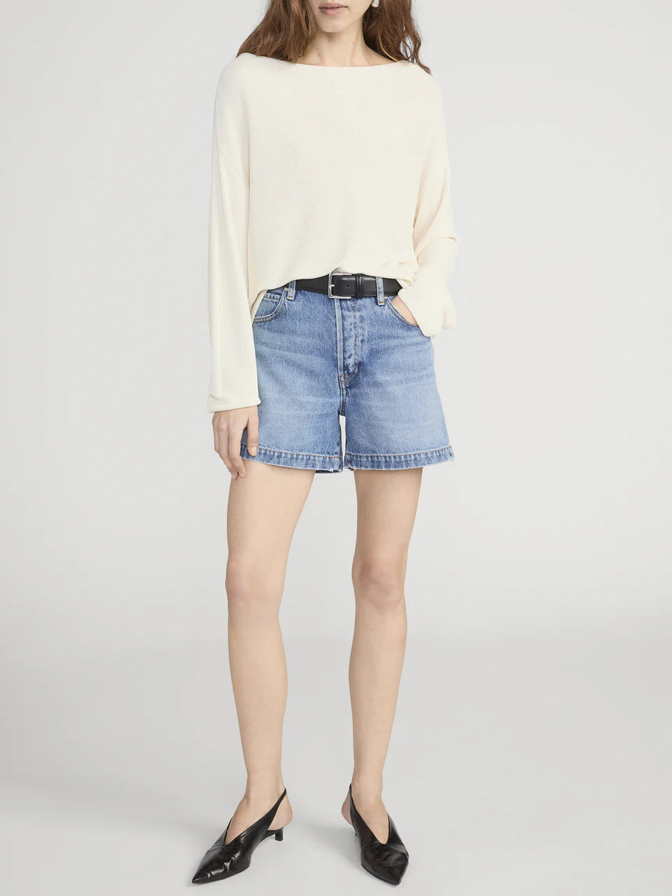 Person wearing a cream sweater and denim shorts on a white background