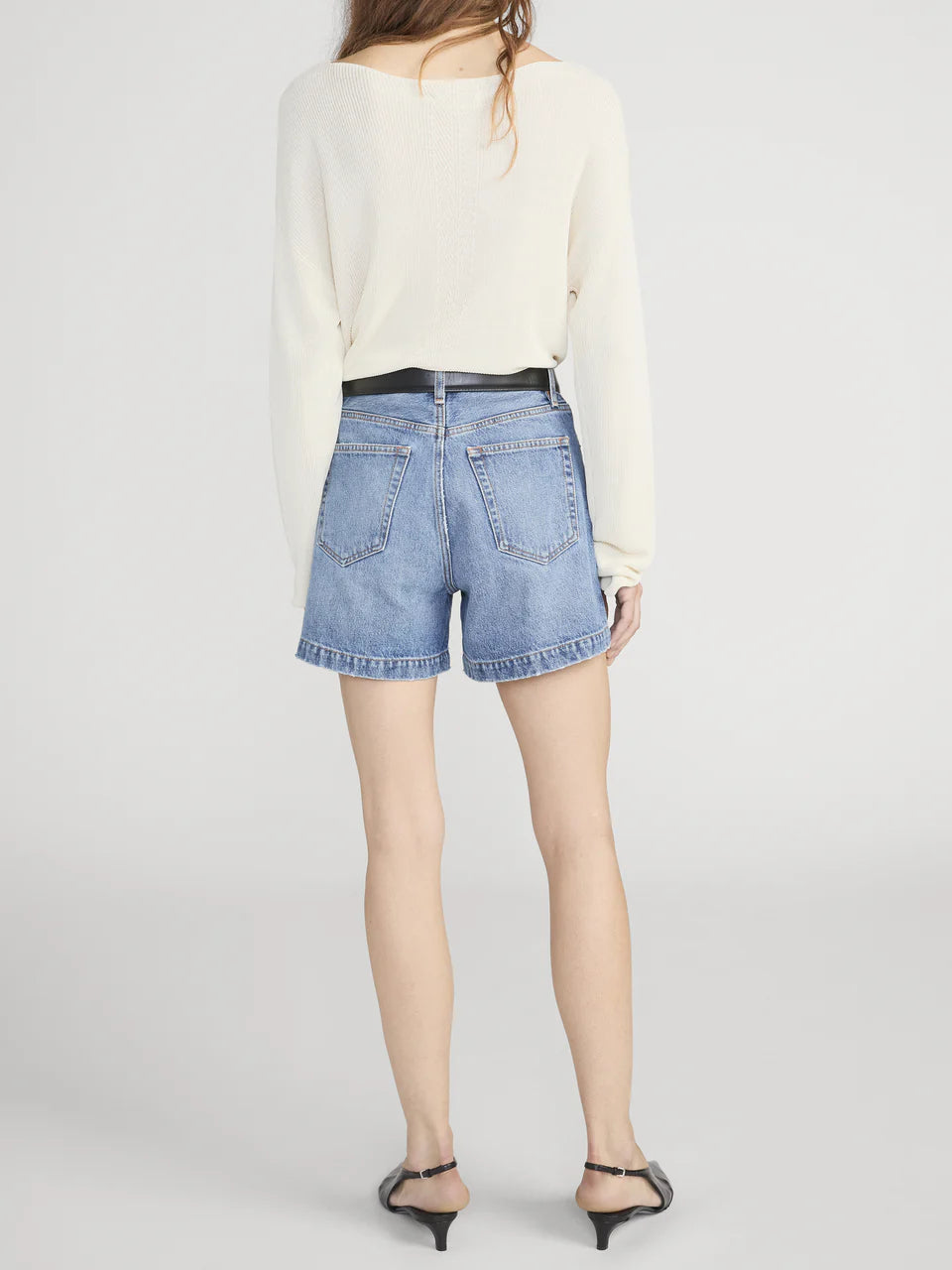 Person wearing a white sweater and blue denim shorts on a plain background