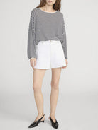 Person wearing a black and white striped sweater with white shorts on a plain background