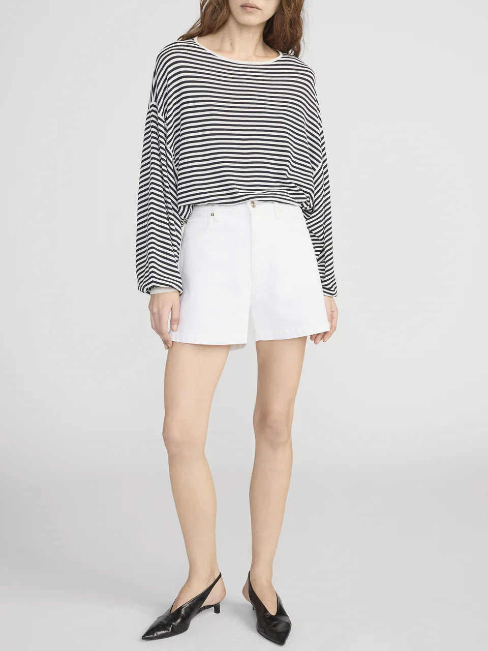 Person wearing a black and white striped sweater with white shorts on a plain background