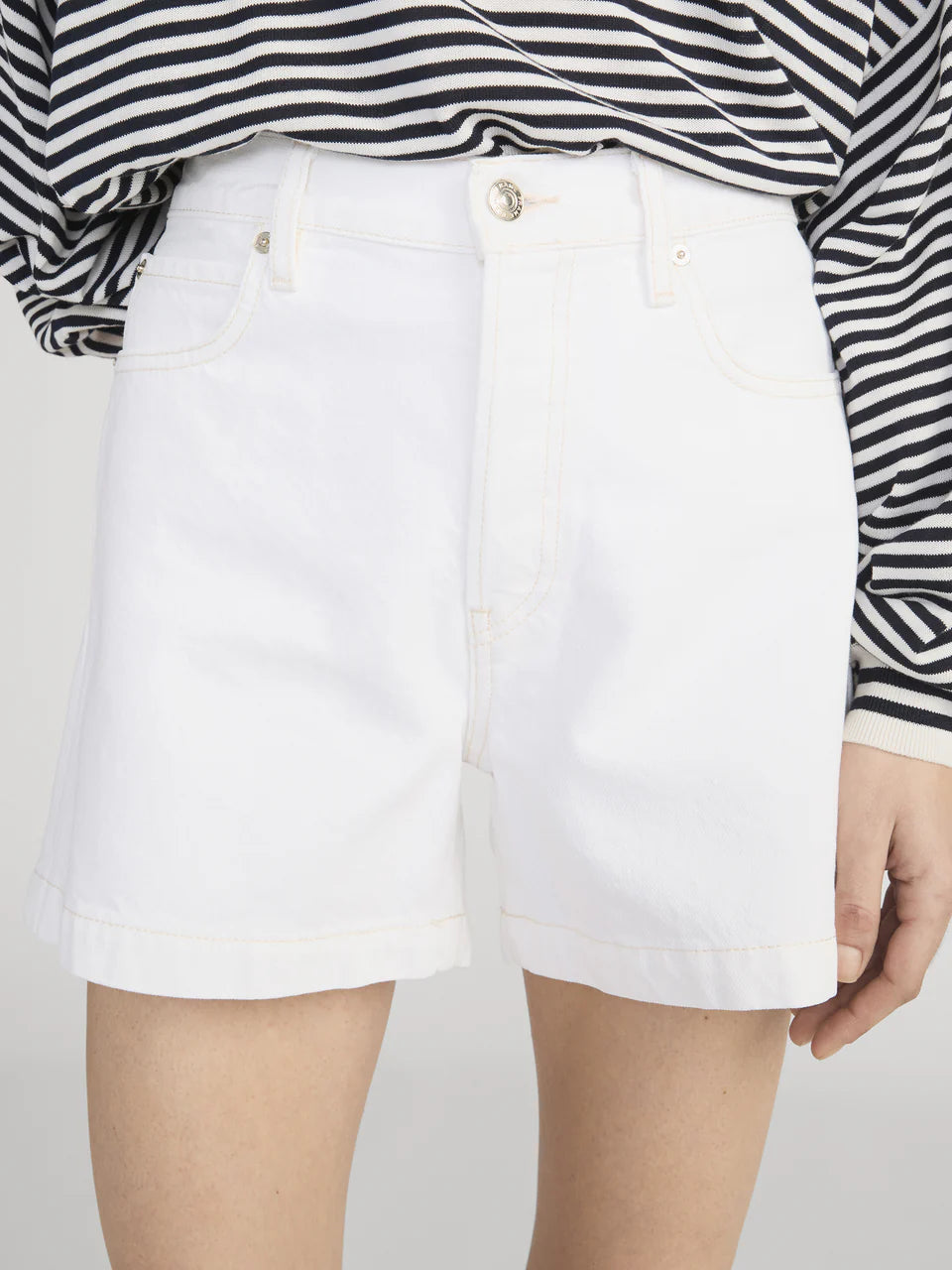 White shorts worn with a black and white striped shirt on a plain background