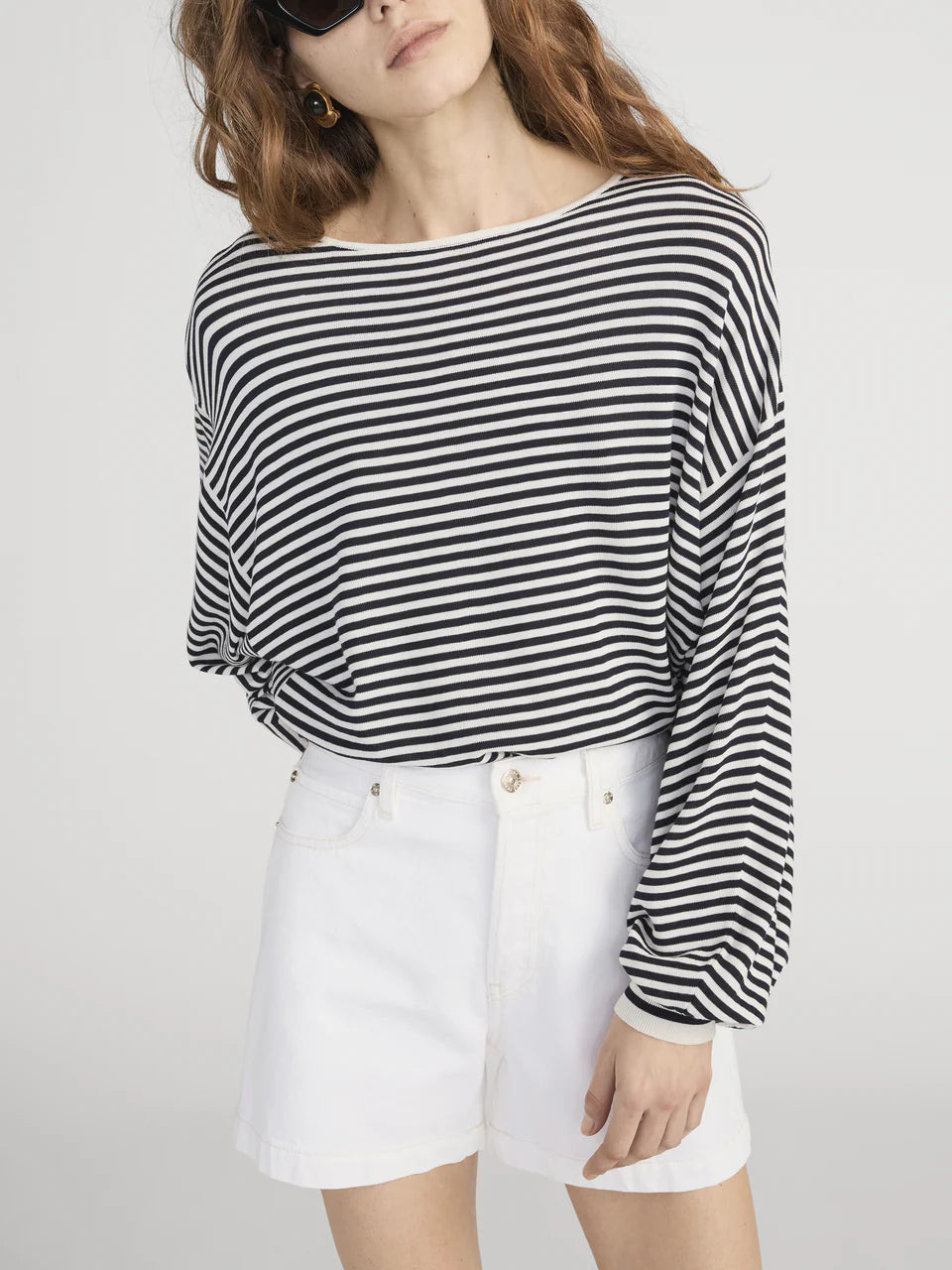 Woman wearing a black and white striped sweater with white shorts on a plain background