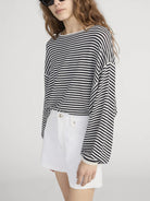 Person wearing a black and white striped long-sleeve top and white shorts on a light gray background