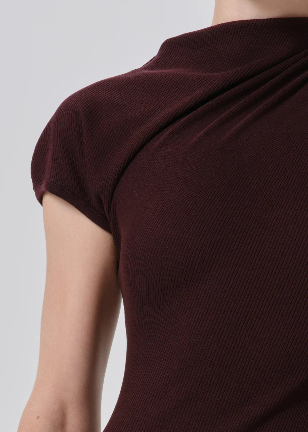 Close-up of a person wearing a ribbed short-sleeve top in deep burgundy, showing the shoulder, arm, and draped neckline against a light gray background.