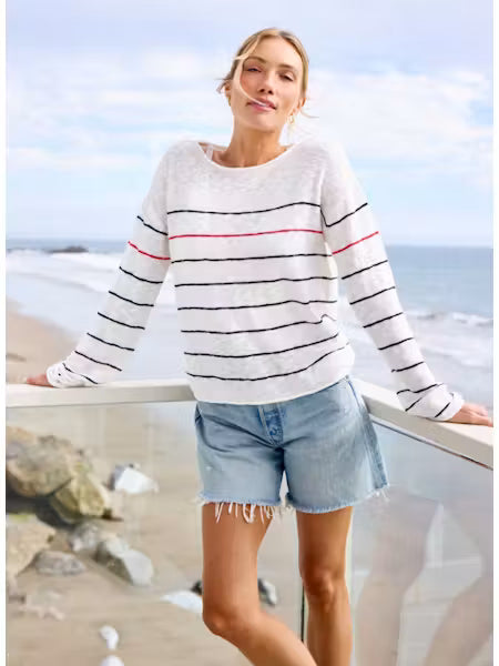 Woman wearing a striped sweater and denim shorts standing on a beach.