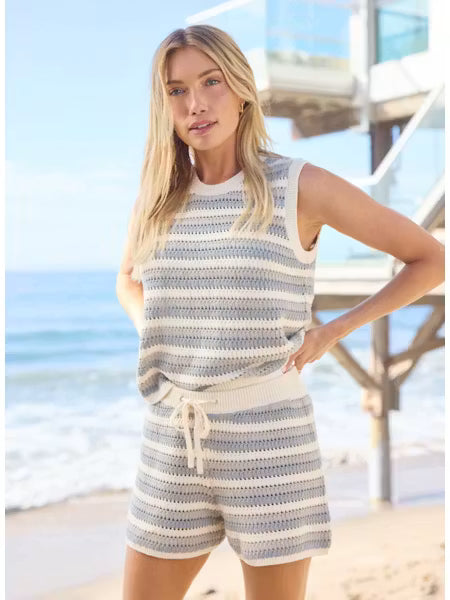 Woman in a striped outfit standing on a beach with ocean and lifeguard tower in the background