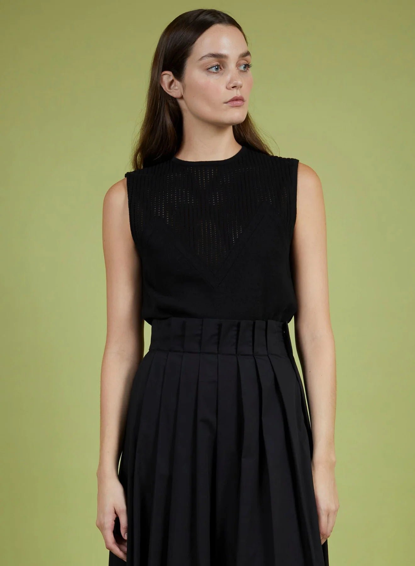 Woman wearing a black sleeveless top and skirt against a green background