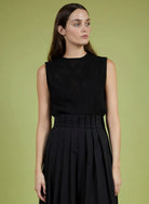 Woman wearing a black sleeveless top and skirt against a green background