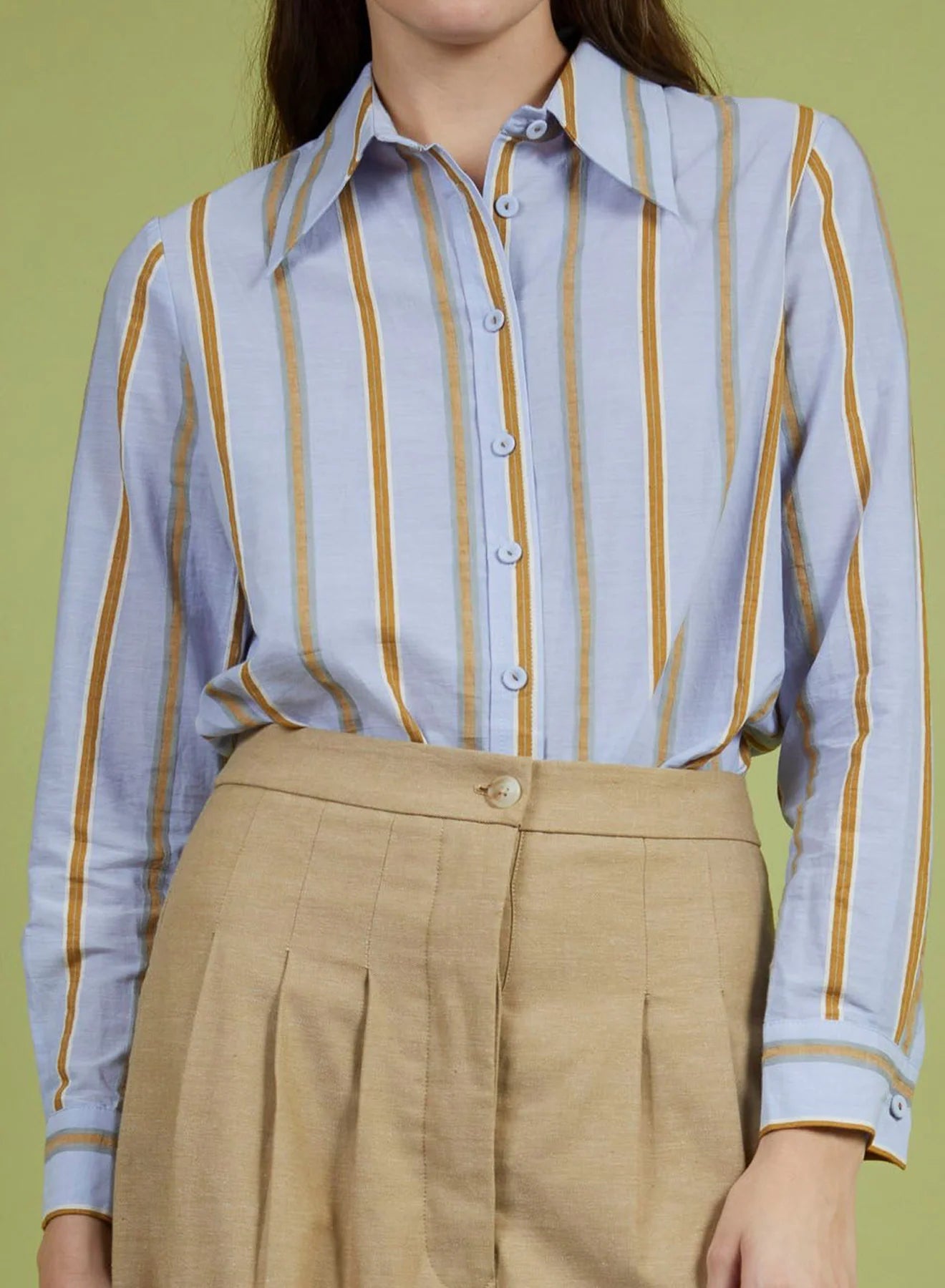 Person wearing a striped shirt with yellow and blue vertical lines and beige pants against a green background