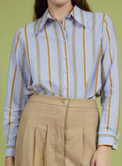 Person wearing a striped shirt with yellow and blue vertical lines and beige pants against a green background