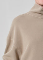 Close-up of a beige sweater with a high collar on a light gray background