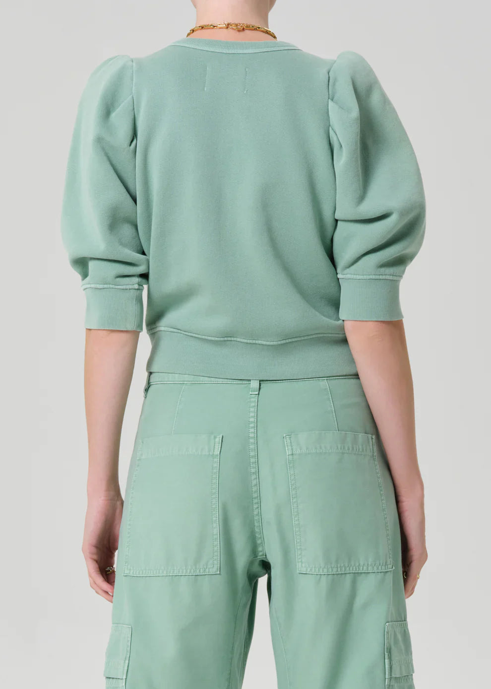 Person wearing a mint green outfit with a matching sweater and pants on a light gray background