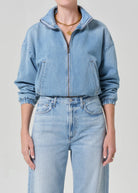 Person wearing a light blue denim jacket and jeans on a plain background