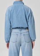 Person wearing a light blue denim jacket and jeans on a plain background