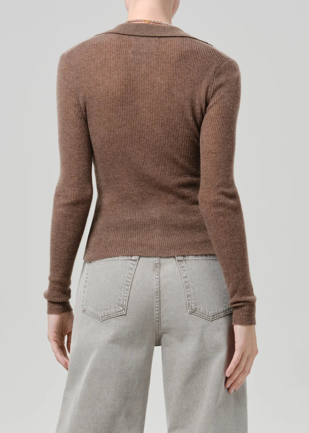 A person shown from the back wearing a fitted ribbed brown long-sleeve knit top and light gray wide-leg jeans against a plain light gray studio background.