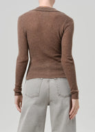 A person shown from the back wearing a fitted ribbed brown long-sleeve knit top and light gray wide-leg jeans against a plain light gray studio background.