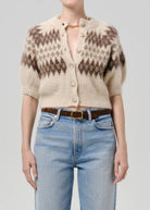 A model wearing a cream and brown patterned short-sleeve knit cardigan with buttons, paired with light blue jeans and a brown belt, against a solid light gray background.
