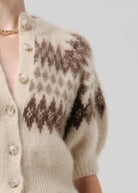 Close-up of a fuzzy knit cardigan worn by a model, featuring a cream base with a brown and beige Fair Isle pattern and cream buttons.