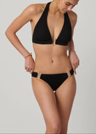 Person wearing a black bikini with gold buckles on a plain background