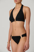 Black bikini with gold accents worn by a model on a plain background